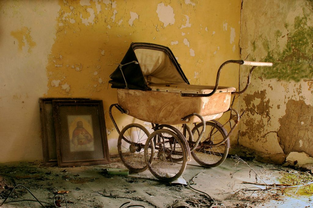 An old pram lies next to a picture of the saviour. The house is empty now and the laughter and cries of the children have long gone.