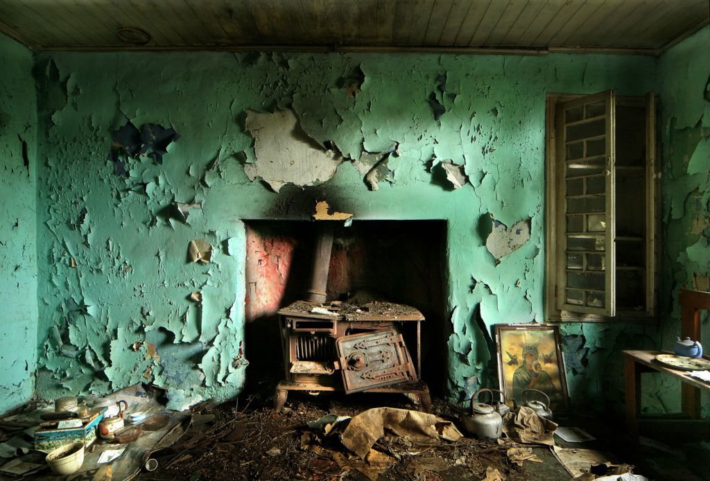 This is of a house in West Cork. Over the years it has become cocooned by surrounding trees that have turned it into a time capsule and makes it almost impossible to see. Inside, a calendar on the wall has a picture of Pope Paul VI dated 1977. In the centre of the kitchen is a solid fuel stove and scattered around the floor are kettles, newspapers and a blue tin of Jacob’s Irish party biscuits decorated with shamrocks, which now contain letters and bills.On top of the tin sits a snow globe and on the right hand side of the stove is a picture of “Our Lady of Perpetual Succour”.