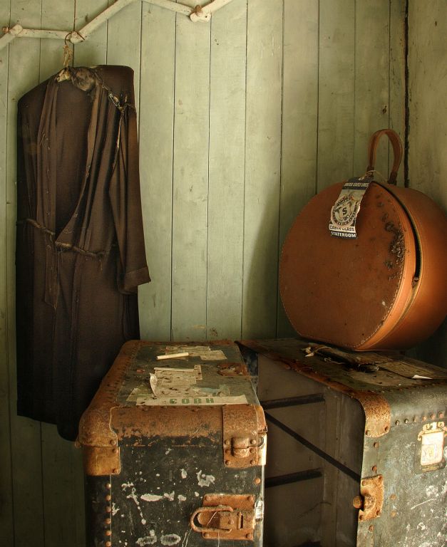  The hatbox has a label for a stateroom on a United States liner while the trunk is marked with the words Cobh. The dress has seen better days and has a safety pin to possibly replace a missing button.