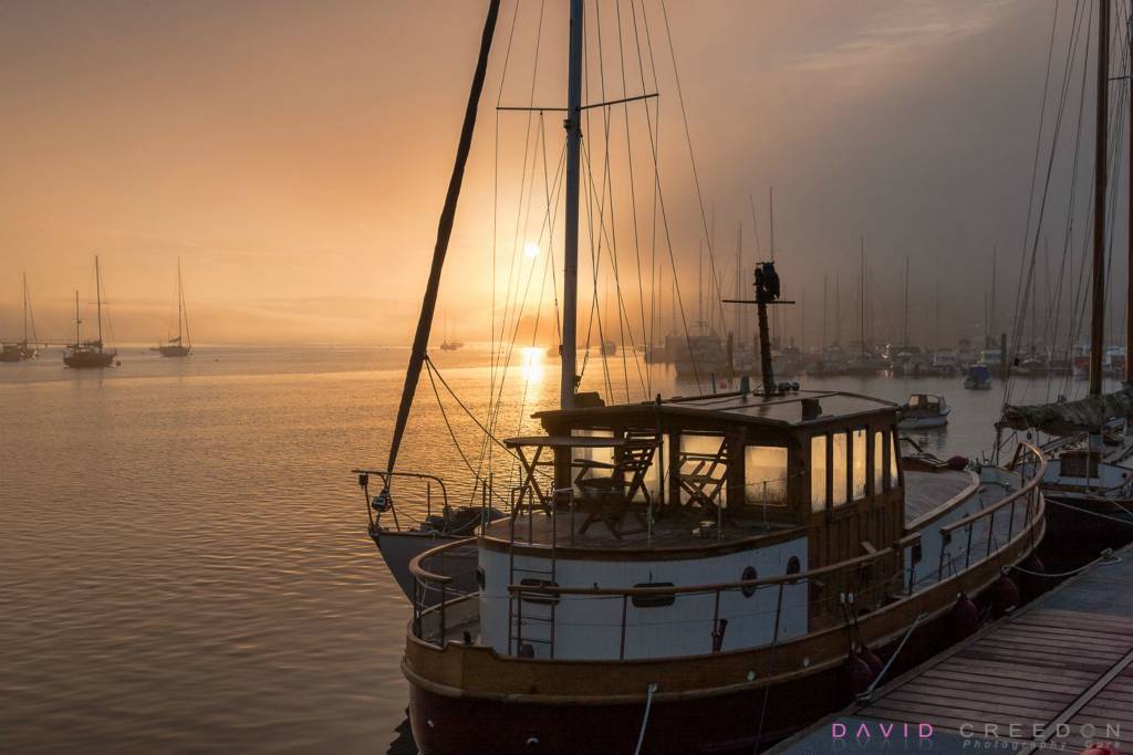 Early morning fog begins to dissipate with the morning sun as the cabin cruiser Naom Lua is tied up at the pier in Crosshaven, Co. Cork, Ireland.