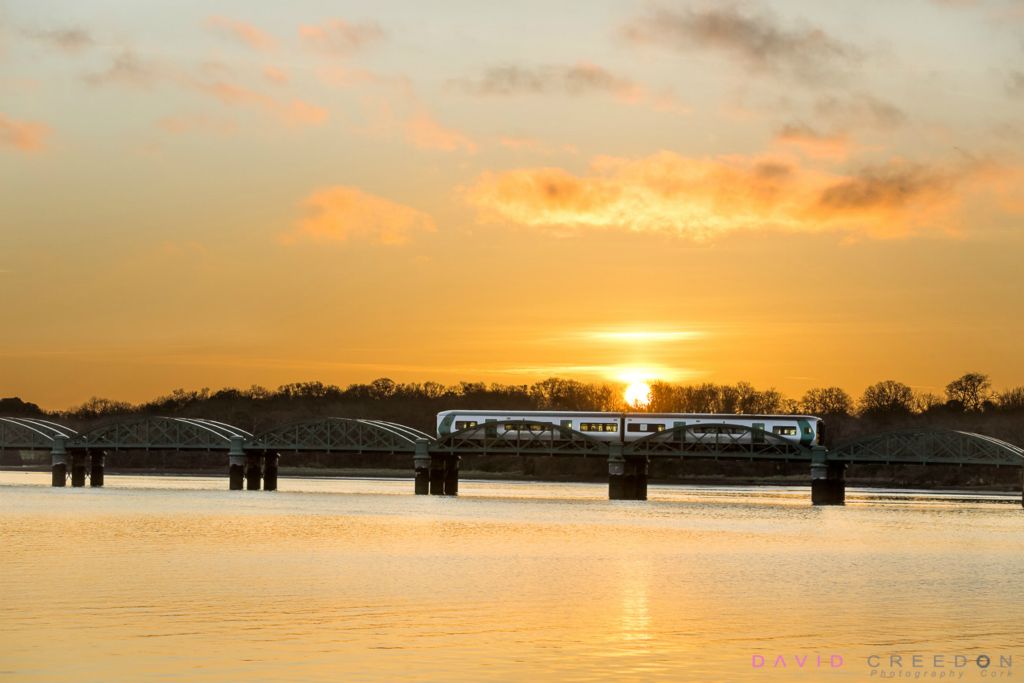 An early morning commuter train from Cobh passes over the iron bridge  as the Sun begins to rise at Fota Island.