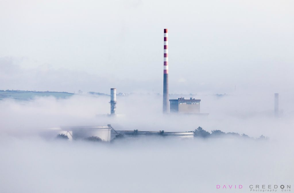 Early morning sun begins to disapate the sea fog that shrouds the storage tanks at the oil refinery and the electric generating station in Aghada, Co. Cork, Ireland. 