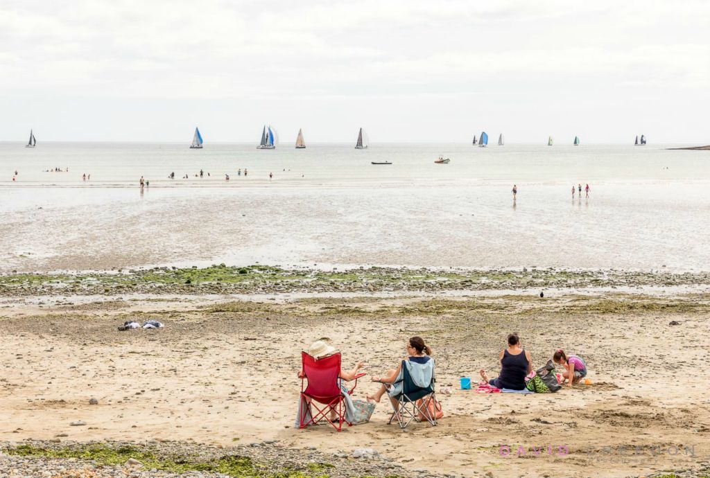 As yachts race offshore during the Volvo Cork Week, holiday makers enjoy the good weather at Fountainstown beach, Co. Cork, Ireland.  